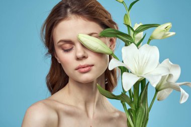 Mavi arka planda beyaz çiçeklerle dolu bir buketi olan çıplak omuzları olan güzel bir kadın.