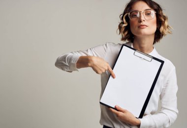 Bir kadın gri bir arka planda beyaz bir sayfa olan bir klasöre bakıyor.