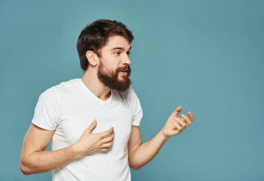 Esmer adam ellerini mavi bir arka planda beyaz bir tişörtle hareket ettiriyor.