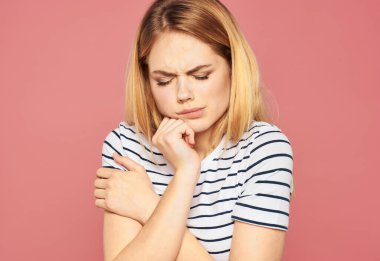 Pembe arka planda çizgili tişörtlü üzgün sarışın kadın.