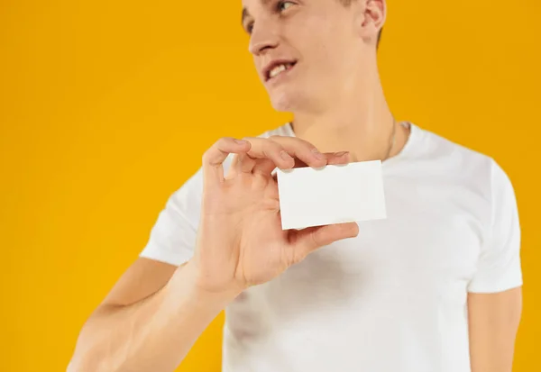 Muž v bílém tričku ukazující vizitku na žlutém pozadí oříznutý pohled — Stock fotografie