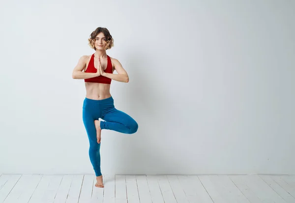 Kvinna gör yoga i ett ljust rum och blå leggings röd tank top — Stockfoto