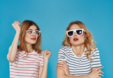 Çizgili tişörtlü iki neşeli kız arkadaş. Güneş gözlükleri, arkadaşlığa sarılıyor. 