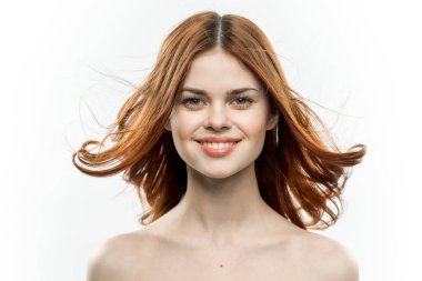 Çıplak omuzlu kızıl saçlı kadın gülümsüyor. Cilt modelini büyülüyor.