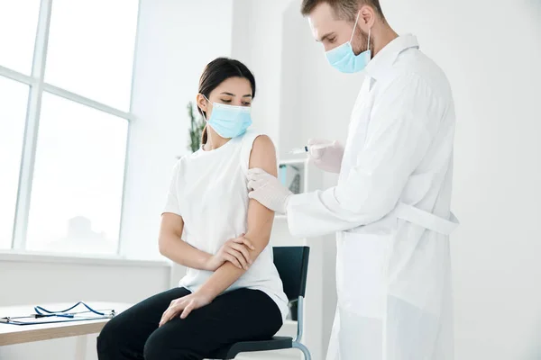 A doctor in a medical gown and a mask injects a female patient in the shoulder covid vaccination — Foto Stock