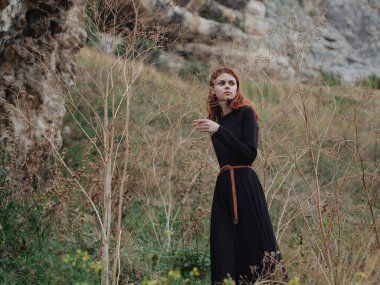 Siyah elbiseli bir kadın sonbaharda ormanda dinleniyor ve ağaç dalları kuru.