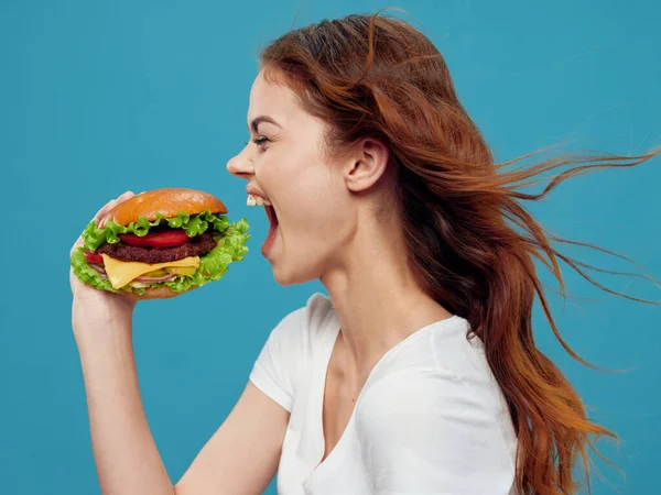Woman drinking hamburger fast food snack close-up blue background — Foto Stock