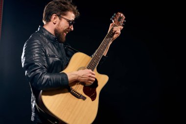 Elinde gitar olan bir adam siyah deri ceket güneş gözlüğü müzik duyguları siyah arka plan