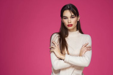 Kırmızı dudaklı, makyajlı beyaz bluzlu, uzun saçlı, pembe arka planlı bir kadın.