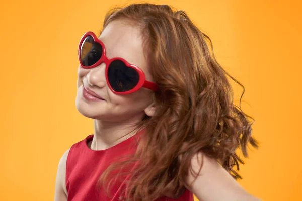 Dziewczyna nosi okulary przeciwsłoneczne w kształcie serca czerwony sukienka studio żółty tło dzieciństwo — Zdjęcie stockowe