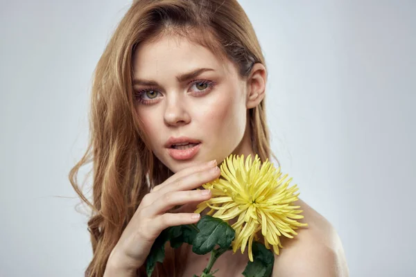 Egy lány sárga virággal, szürke háttérrel néz előre közelkép portré — Stock Fotó