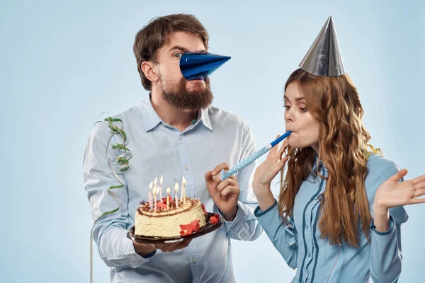 Homem e mulher celebram aniversário com bolo e em chapéus no fundo azul — Fotografia de Stock