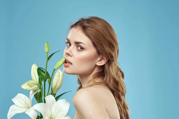 Kobieta z bukietem białych kwiatów na niebieskim tle nagie ramiona piękna twarz — Zdjęcie stockowe