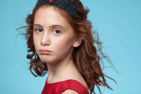 Mała dziewczynka z kręconymi włosami z koroną na głowie czerwona sukienka Uśmiech niebieskie tło — Zdjęcie stockowe