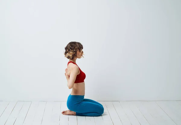 En kvinna i blå leggings sitter på ett ljust golv inomhus och håller händerna bakom ryggen — Stockfoto