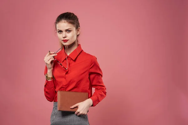 Mujer de negocios en una camisa roja elegante fondo rosa con un cuaderno en sus manos — Foto de Stock