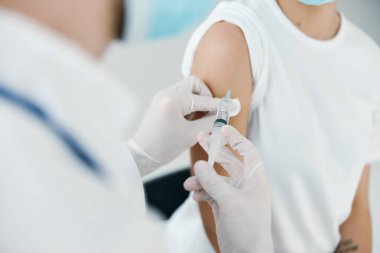 Doktor, bir kadının omzuna yakın plan bir iğne yapıyor.