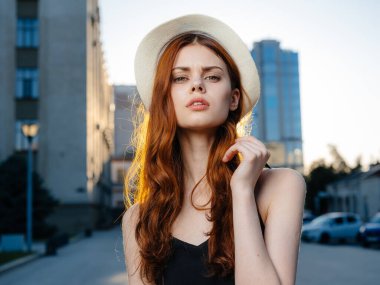 Siyah elbiseli ve şapkalı romantik bir kadın, şehirdeki yüksek binaların yakınında fotoğraflanır.