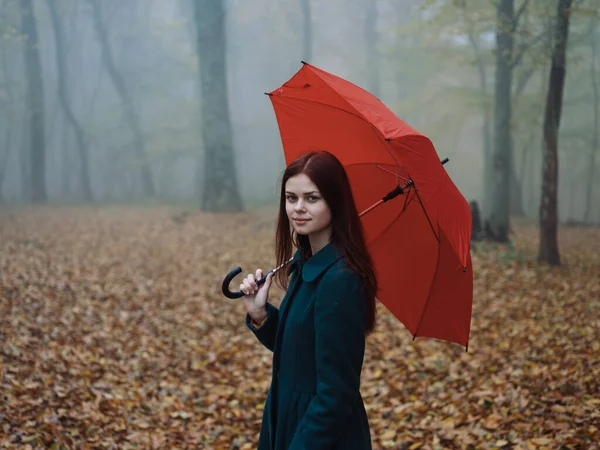Hübsche Frau mit rotem Regenschirm im Herbst auf naturgelben Blättern spazieren — Stockfoto