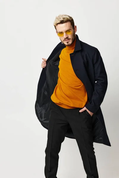 Atractivo hombre moda peinado gafas negro abrigo luz fondo — Foto de Stock