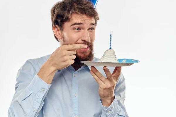 Un hombre celebra un cumpleaños sobre un fondo claro con un pastel en un plato gorra divertida flauta — Foto de Stock