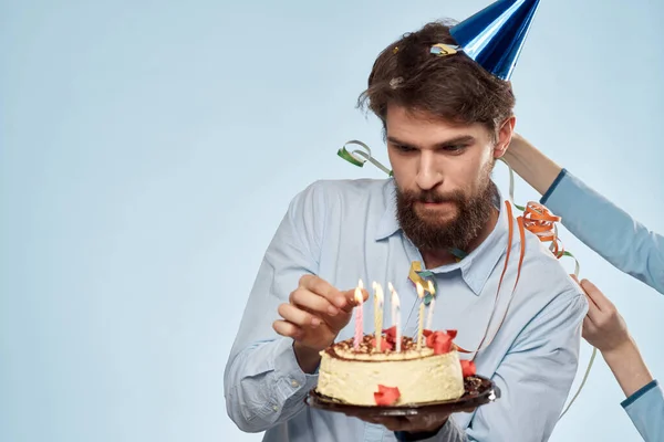 Человек с тарелкой торта и праздничной корпоративной вечеринкой с голубыми свечами на заднем плане — стоковое фото