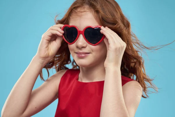 Güneş gözlüklü küçük kız kupa şeklinde kırmızı elbise kıvırcık saç mavi arka plan — Stok fotoğraf