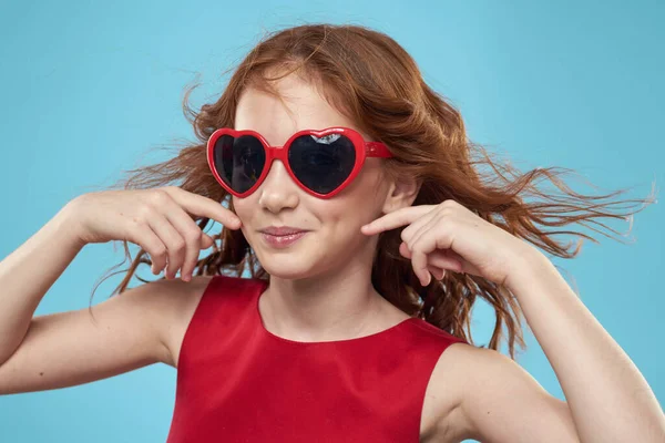 Petite fille en lunettes de soleil sous la forme de coeurs robe rouge cheveux bouclés fond bleu — Photo