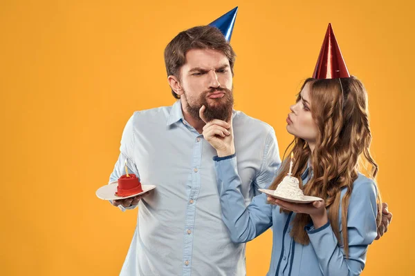 노란 배경 뷰에 케이크가 그려진 모자를 쓴 생일 파티 남자와 여자 — 스톡 사진