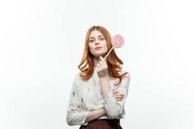Kızıl saçlı güzel bir kadın lolipop şeker tutuyor ve şekerlerin tadını çıkarıyor.