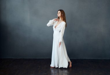 Beyaz elbiseli hoş bir bayan arka planda dans ediyor. El modeliyle el kol hareketi yapıyor.