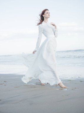 Okyanusun yanındaki beyaz elbiseli kadın çıplak ayak portresi.