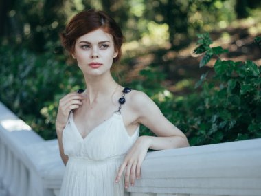 Beyaz elbiseli kadın cazibeli taze hava yeşil yapraklı yürüyüş modeli