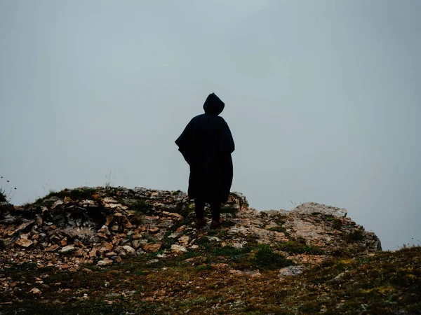 Un hombre camina en la naturaleza en las montañas con un abrigo negro y una capucha —  Fotos de Stock