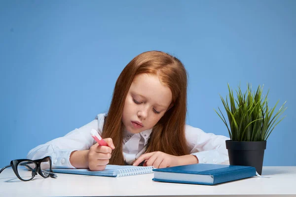 赤い髪の少女は教科書の授業でテーブルに座り — ストック写真