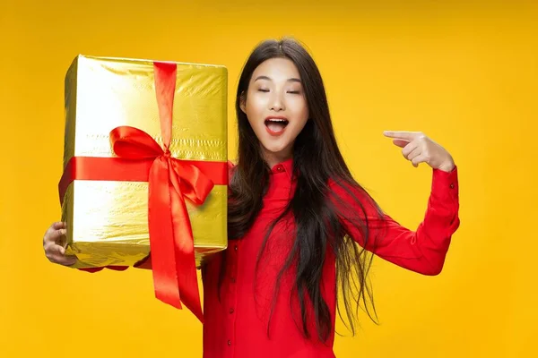 surprised woman with gift box on yellow background shows finger to the side