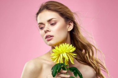 Çıplak omuzları olan güzel bir kadın ve pembe arka planda sarı bir çiçek.