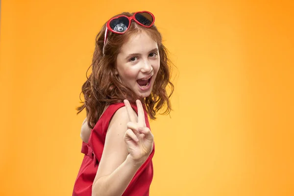 Menina em óculos pretos vestido vermelho infância divertido fundo amarelo — Fotografia de Stock