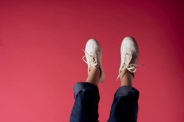 Ters dönmüş kadın bacakları beyaz spor ayakkabılar, sokak tarzı pembe arka plan.