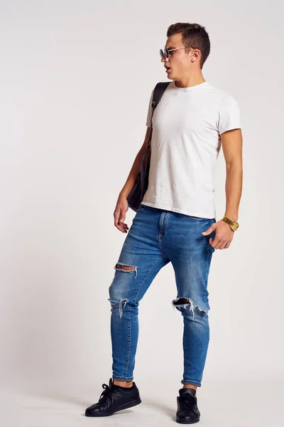 Een man met een rugzak op zijn rug in jeans t-shirt full length sneakers en bril op zijn gezicht — Stockfoto