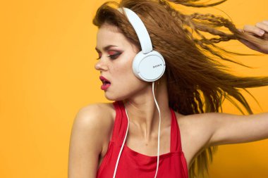 Kulaklık takan, müzik dinleyen kırmızı tişört giyen, duyguları sarı arka planda olan bir kadın.