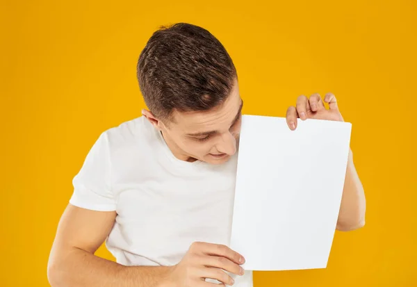 Zakenman met een wit vel papier op een gele achtergrond reclame blanco visitekaartje — Stockfoto