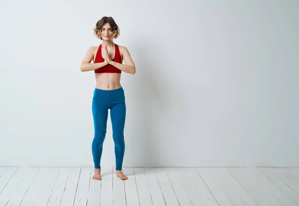 Жінка робить йогу в світлій кімнаті і синіх легінсах червоний бак зверху — стокове фото