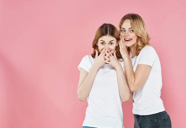 Mujeres alegres en camisetas blancas abrazos socializar estilo de vida Glamor fondo rosa — Foto de Stock