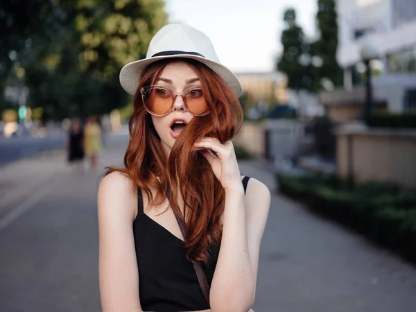 La mujer a la moda en el vestido negro y en el sombrero blanco descansan en la naturaleza en la calle en el parque — Foto de Stock