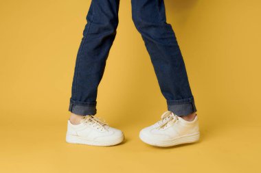 Şık ayakkabılar beyaz spor ayakkabılar, bacaklar sarı arka plan kırpılmış manzara.