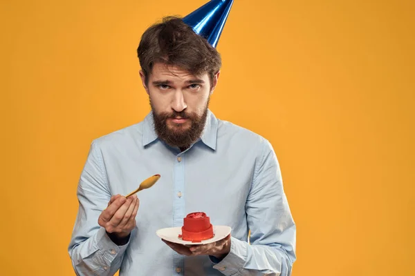 Мужчина с праздничным тортом в руках и в кепке на жёлтом фоне в свой день рождения — стоковое фото