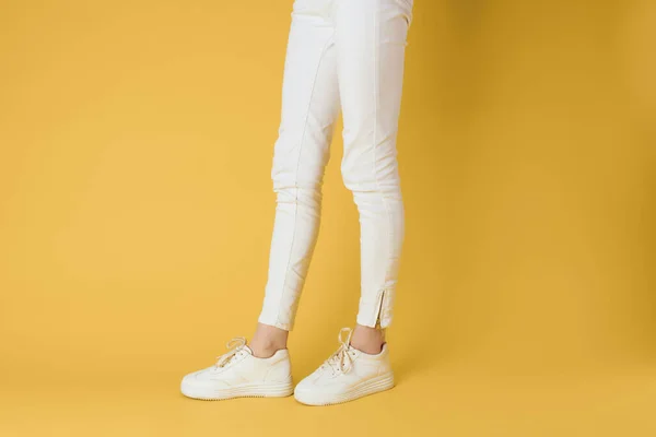 Pies femeninos zapatillas blancas aspecto atractivo moda fondo amarillo —  Fotos de Stock