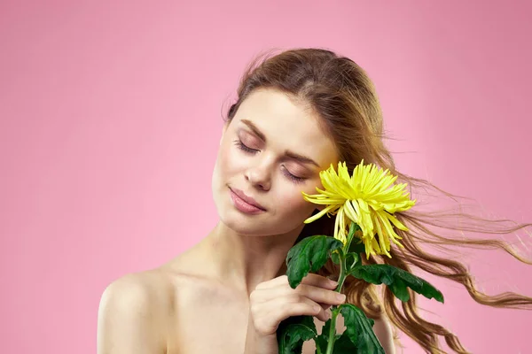 Krásná dívka se žlutou květinou na růžovém pozadí nahé ramena make-up — Stock fotografie