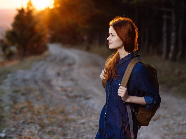 Woman on the road with a sunset sun backpack and forest in the background